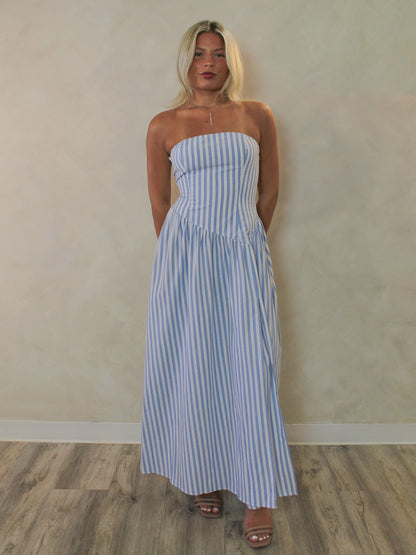 a woman wearing a vertical stripe, blue and white, strapless maxi dress.