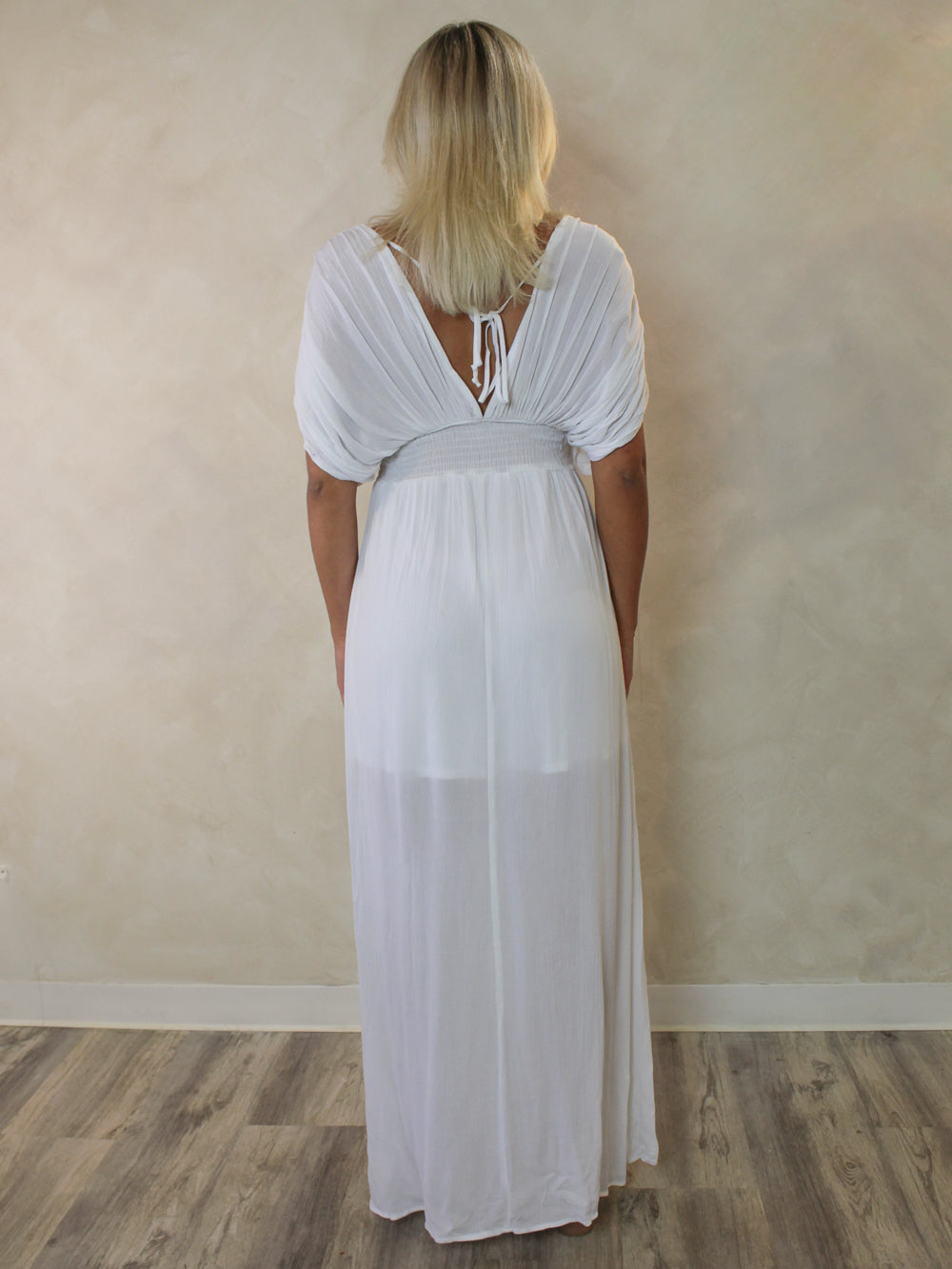 A woman viewed from behind wearing a white maxi dress with short puff sleeves, a tie-back neckline