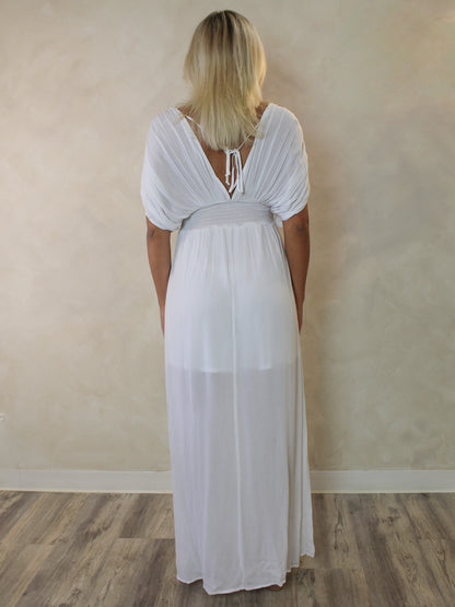 A woman viewed from behind wearing a white maxi dress with short puff sleeves, a tie-back neckline