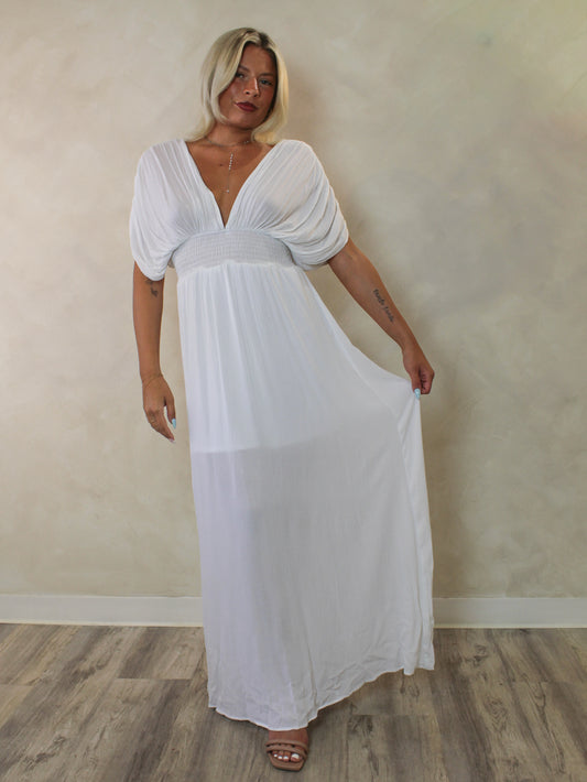 White maxi dress with a deep v neckline, draped sleeves, smocked waist and a flowing skirt