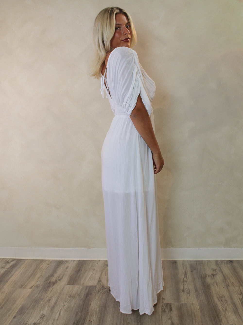 A woman with blonde hair wearing a white maxi dress with draped short sleevs