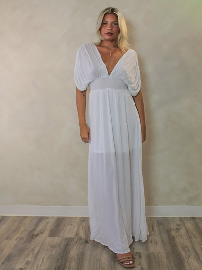 A woman modeling a white maxi dress with a deep V-neckline, short draping sleeves, and a flowing skirt.