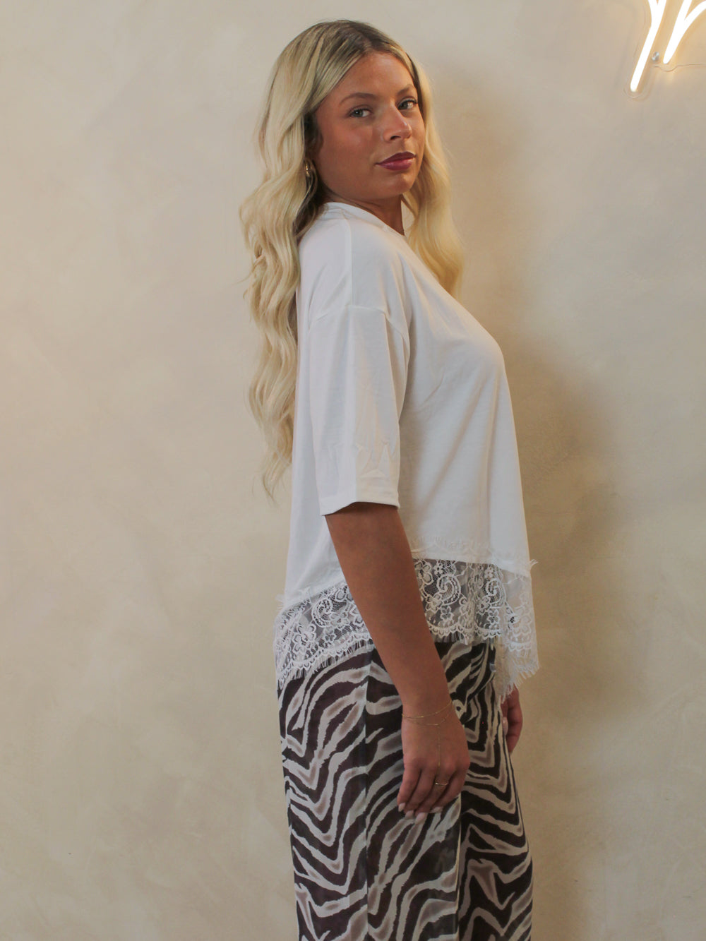 Model wearing a white tee with a lace trim hem and styled with zebra pants