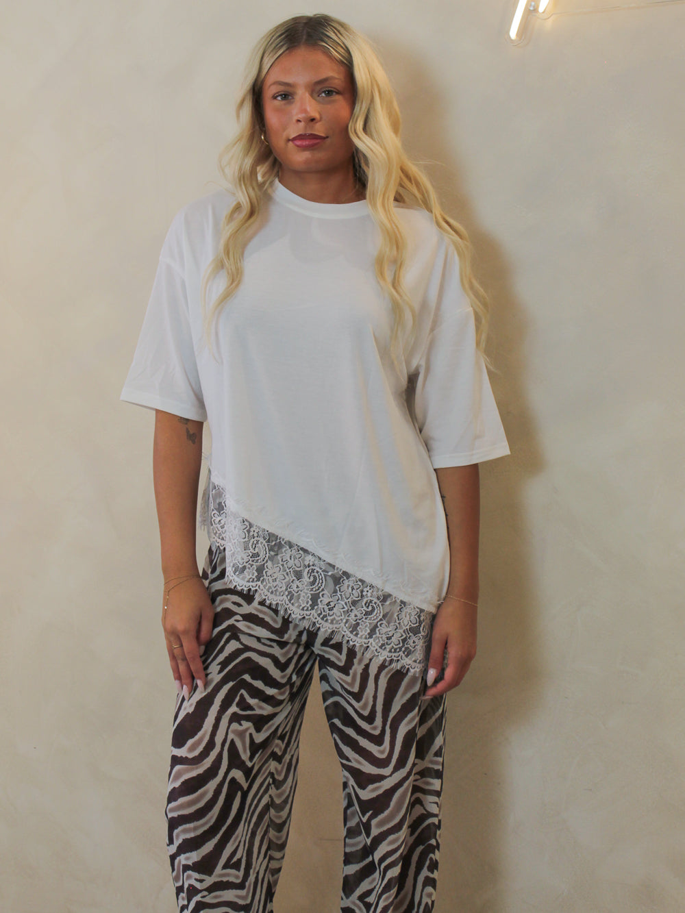 Model wearing a white oversized tee with an asymmetric lace trim and paired with zebra pants.