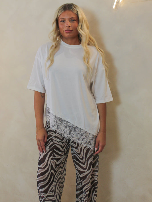 Model wearing a white oversized tee with an asymmetric lace trim and paired with zebra pants.