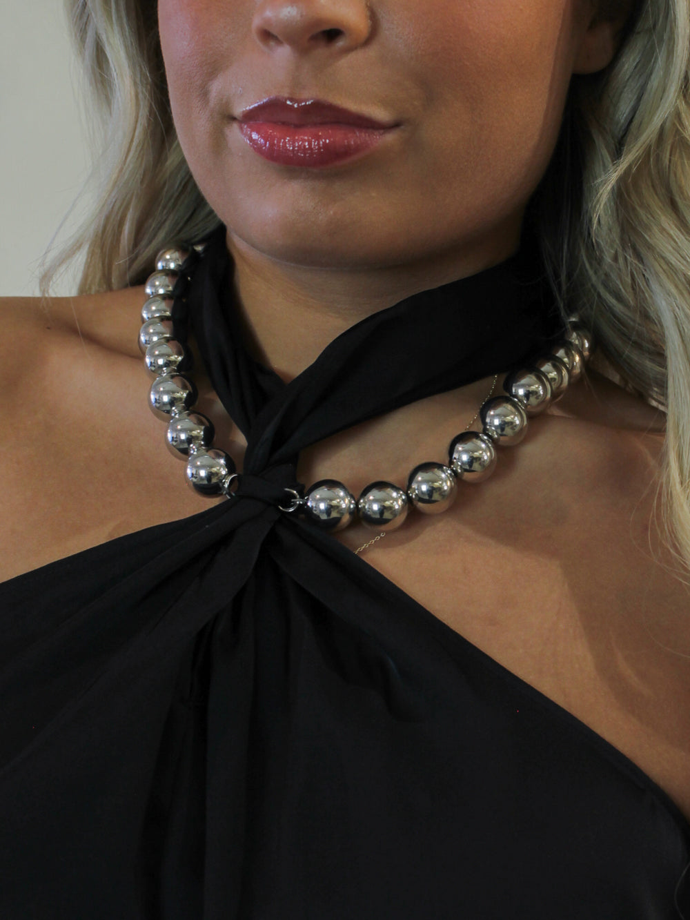 Model wearing a black halter top with a chunky silver necklace attached at the neckline 