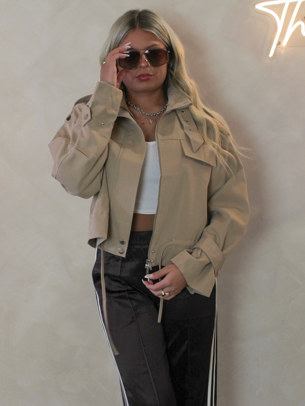 Model wearing a tan cropped, trench coat with sunglasses and brown stripe pants 