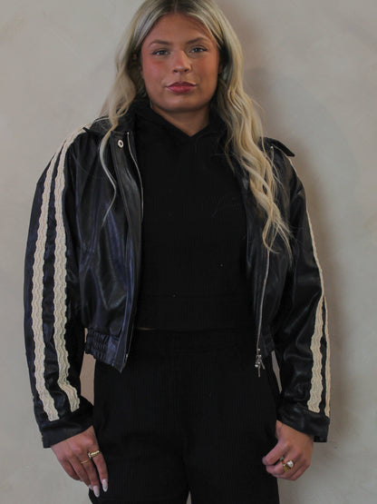 Model wearing a black, faux leather jacket with lace trim details 