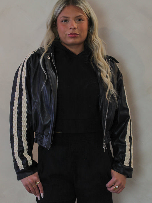 Model wearing a black, faux leather jacket with lace trim details 
