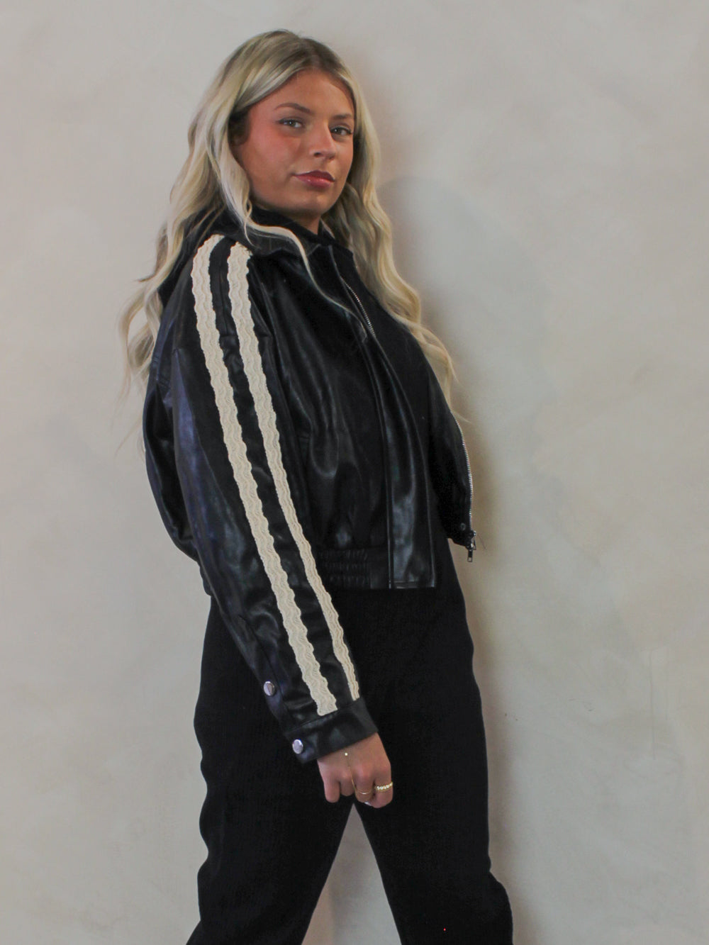 Model wearing a black faux leather bomber jacket with lace trim sleeve details 