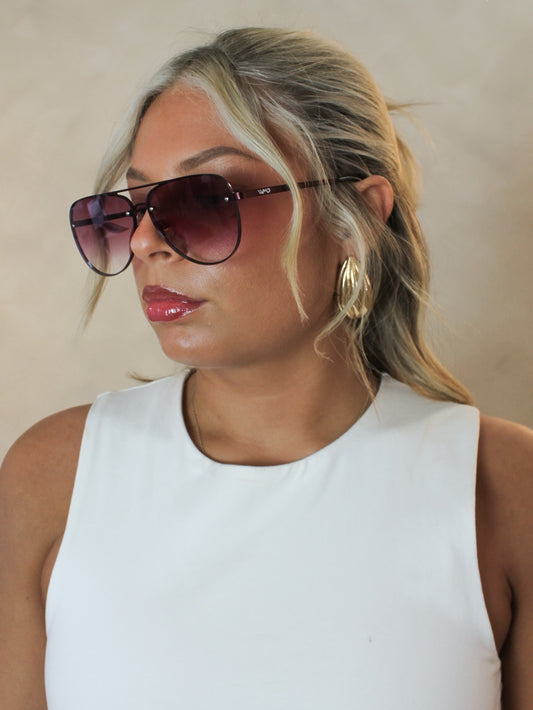 Woman wearing oversized aviator sunglasses with a rimless look, gradient burgundy lenses and matching metal frame. 
