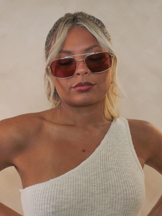 Woman wearing gold rimmed sunglasses with warm coral color lenses