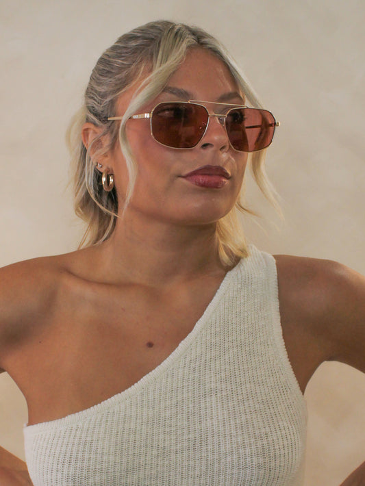 Woman wearing gold rimmed sunglasses with coral lenses
