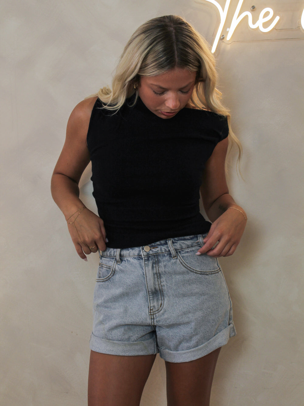 Woman wearing a black short sleeve off the shoulder top styled with denim shorts