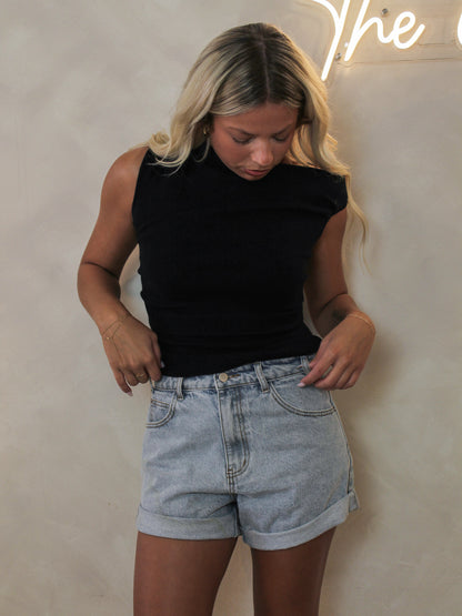 Woman wearing a black short sleeve off the shoulder top styled with denim shorts